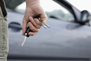 Close up of a man holding car keys and a car in the background